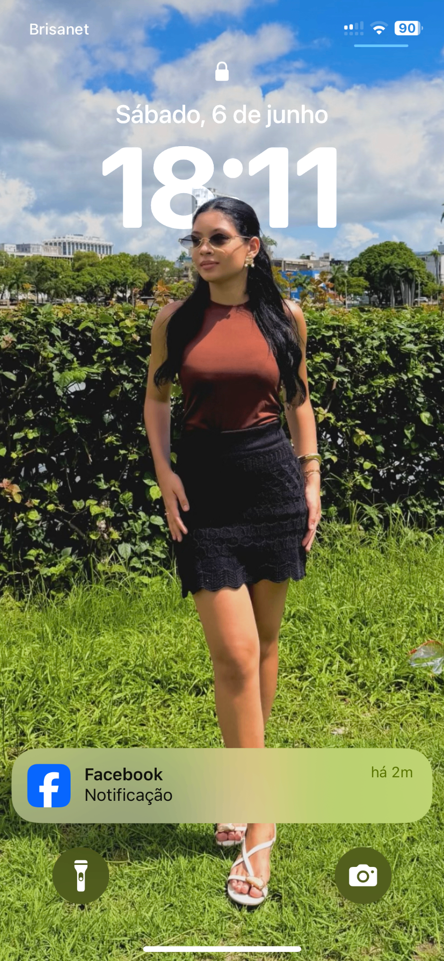 Foto ao ar livre com look marrom e preto, debaixo de um céu azul bonito.